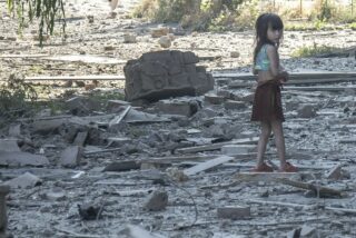 A small child walks through concrete and metal debris from an explosion.